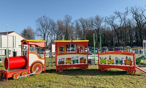 Zdjęcie drewnianej i kolorowej lokomotywy z wagonikami postawionej na placu zabaw